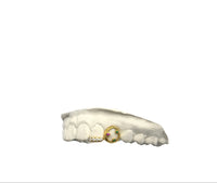 A set of gold-colored grillz with one tooth featuring three gemstones and the other with a diamond strip, on a white background.